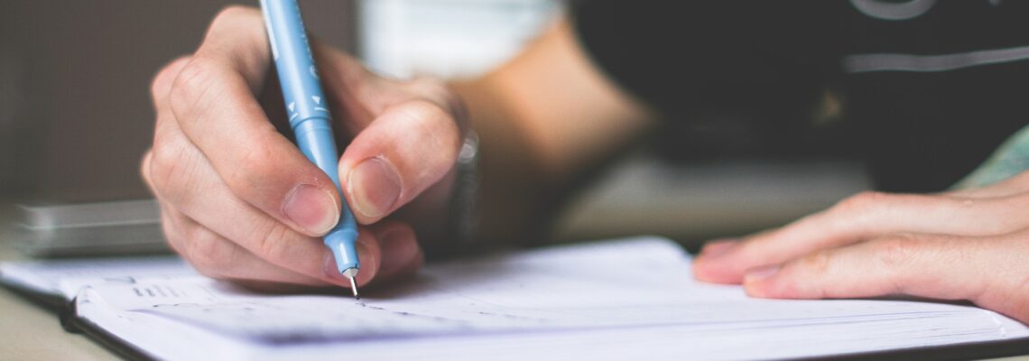 Person writing in notebook with pen